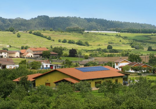 Casa con paneles solares en el tejado rodeada de una pradera de color verde
